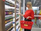 Mulher loira olhando para uma prateleira de produtos e segurando uma cesta do supermercado Fort Atacadista